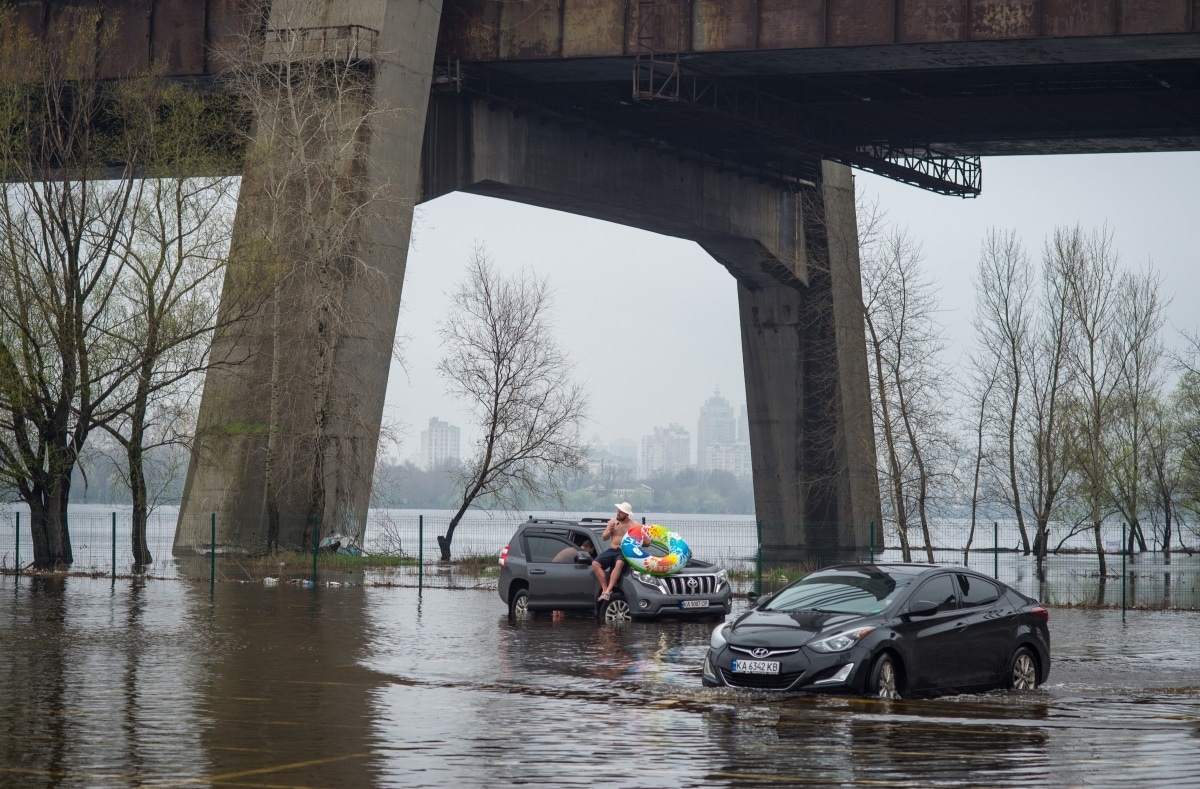 "Kyiv, Kyiv region Ukraine - 04.15.2023: Flooded parking lot near a bridge, cars drive on water and people swim in flooded parking lot.".