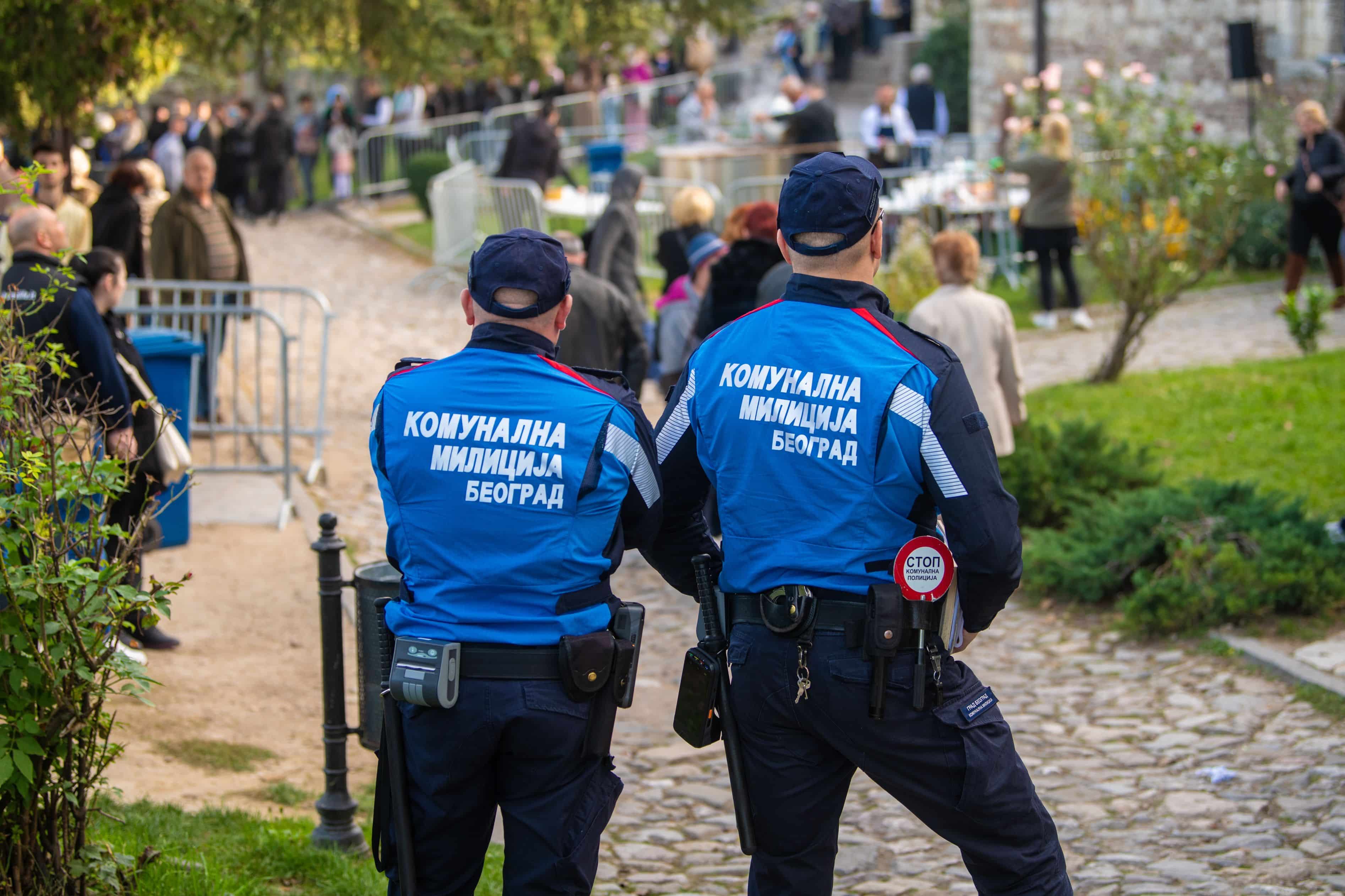 Two Police officers observing an outdoor public event, crowd of people in background. View from behind. Belgrade, Serbia 27.10.2022 Translation: ''Communal Police''