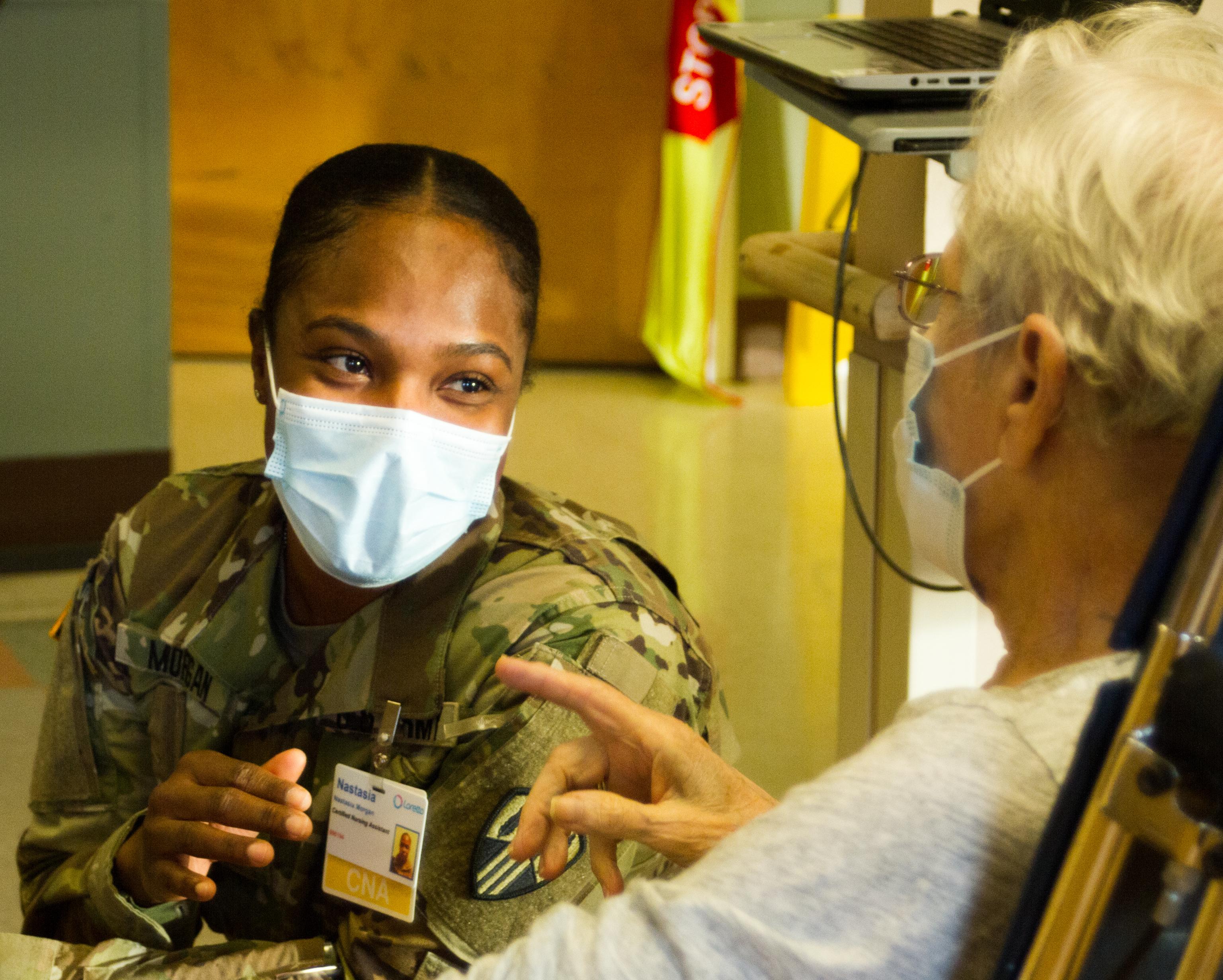 SYRACUSE--Pvt. Nastasia Morgan, a combat medic assigned to the 107th Military Police Company, 369th Sustainment Brigade, sits with a resident at Loretto Health and Rehab in Syracuse, NY Dec. 20. As part of New York State's response to Covid-19, National Guard medics have been deployed in nursing homes to help alleviate congestion of the state’s healthcare system (U.S. Army photo by Staff Sgt. Alexander Rector / released).